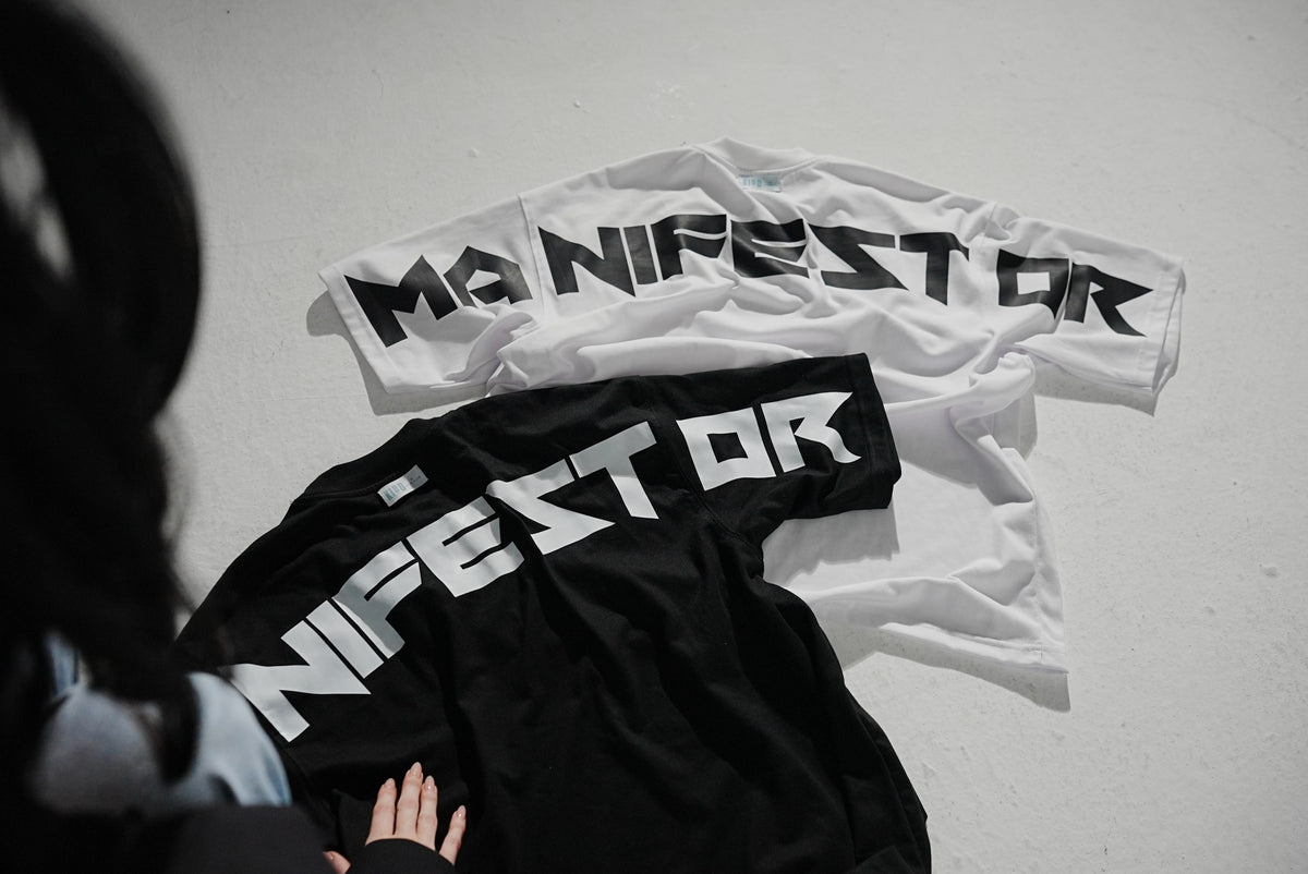 The Manifestor tee in white and black, laid flat with the back print facing up