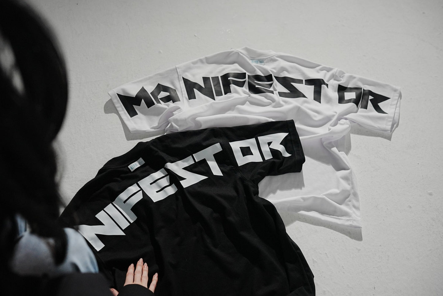 The Manifestor tee in white and black, laid flat with the back print facing up